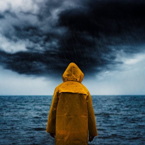 Back of person wearing yellow raincoat, looking over stormy sea.