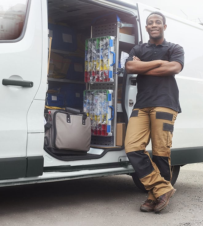 A young male technician leaning against a full stocked service truck.